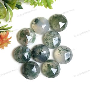 May include: Nine round, faceted moss agate gemstones are displayed. The gemstones feature a mix of translucent white, green, and brown hues. Each stone has a unique pattern, with visible inclusions resembling moss. The gemstones are arranged on a white surface.