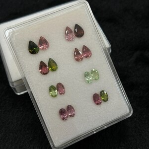 May include: A clear plastic box containing 10 pear-shaped gemstones. The gemstones are in pairs of pink, green, and brown.