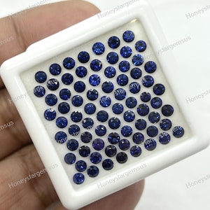Könnte beinhalten: Nahaufnahme eines weißen Tabletts, gefüllt mit 100 runden, blauen Saphir-Edelsteinen. Die Edelsteine sind in einem Gittermuster angeordnet.