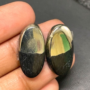 May include: Two oval-shaped cabochons, one half is a shiny gold pyrite and the other half is a black stone.