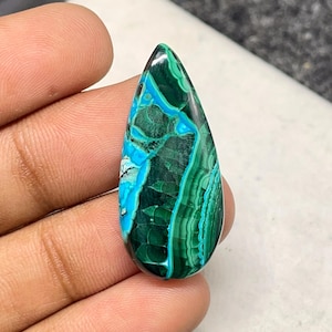 May include: A teardrop-shaped cabochon of green and blue chrysocolla, a natural gemstone with a swirling, layered pattern.