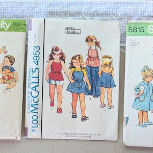 May include: Three vintage sewing pattern envelopes for children's clothing. The left envelope is Simplicity 5531, the center is McCall's 4953, and the right is Simplicity 5815. Each envelope displays illustrations of children wearing various outfits.