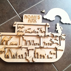 May include: Wooden Noah's Ark puzzle with a rainbow and various animal pieces, including a camel, giraffe, elephant, and a rooster. The puzzle is labeled "Noah's Ark".