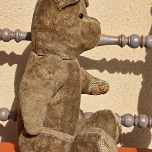 K&ouml;nnte beinhalten: Ein vintage Pl&uuml;sch-Teddyb&auml;r in Braun mit einem schwarzen Knopfauge. Der B&auml;r sitzt auf einer roten Oberfl&auml;che.