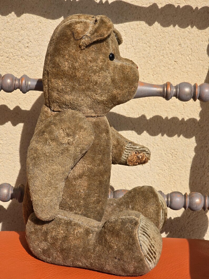 K&ouml;nnte beinhalten: Ein vintage Pl&uuml;sch-Teddyb&auml;r in Braun mit einem schwarzen Knopfauge. Der B&auml;r sitzt auf einer roten Oberfl&auml;che.