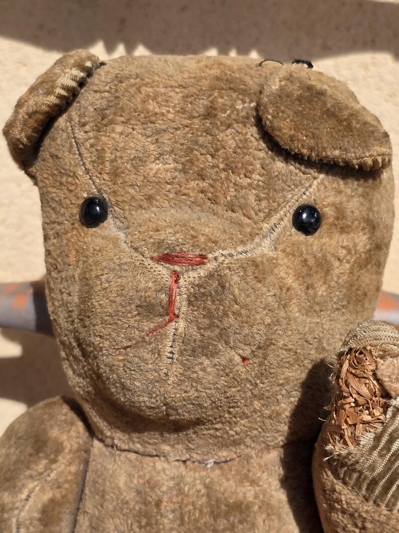 K&ouml;nnte beinhalten: Ein vintage brauner Teddyb&auml;r mit schwarzen Knopfaugen und einer roten gestickten Nase. Der B&auml;r ist aus Pl&uuml;schstoff gefertigt und hat ein abgenutztes Aussehen.