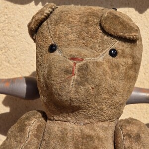 K&ouml;nnte beinhalten: Ein brauner Vintage-Teddyb&auml;r mit schwarzen Knopfaugen und einer roten gestickten Nase. Der B&auml;r sitzt auf einem Holzstuhl.