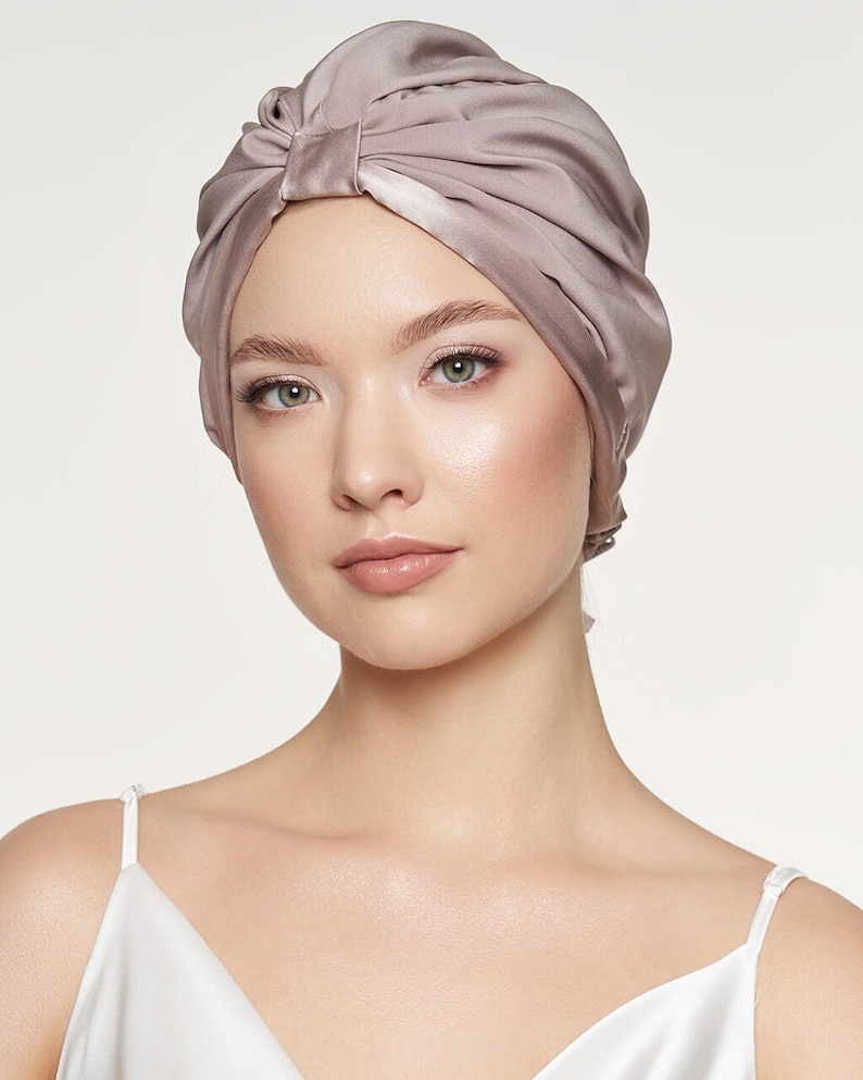 May include: A woman wearing a light brown satin turban. The turban is tied in a knot at the top of her head.