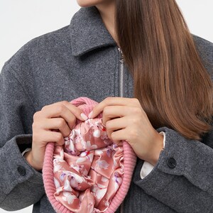 Puede incluir: Un gorro de punto rosa con forro de estampado floral. El gorro lo sostiene una persona que lleva una chaqueta gris.