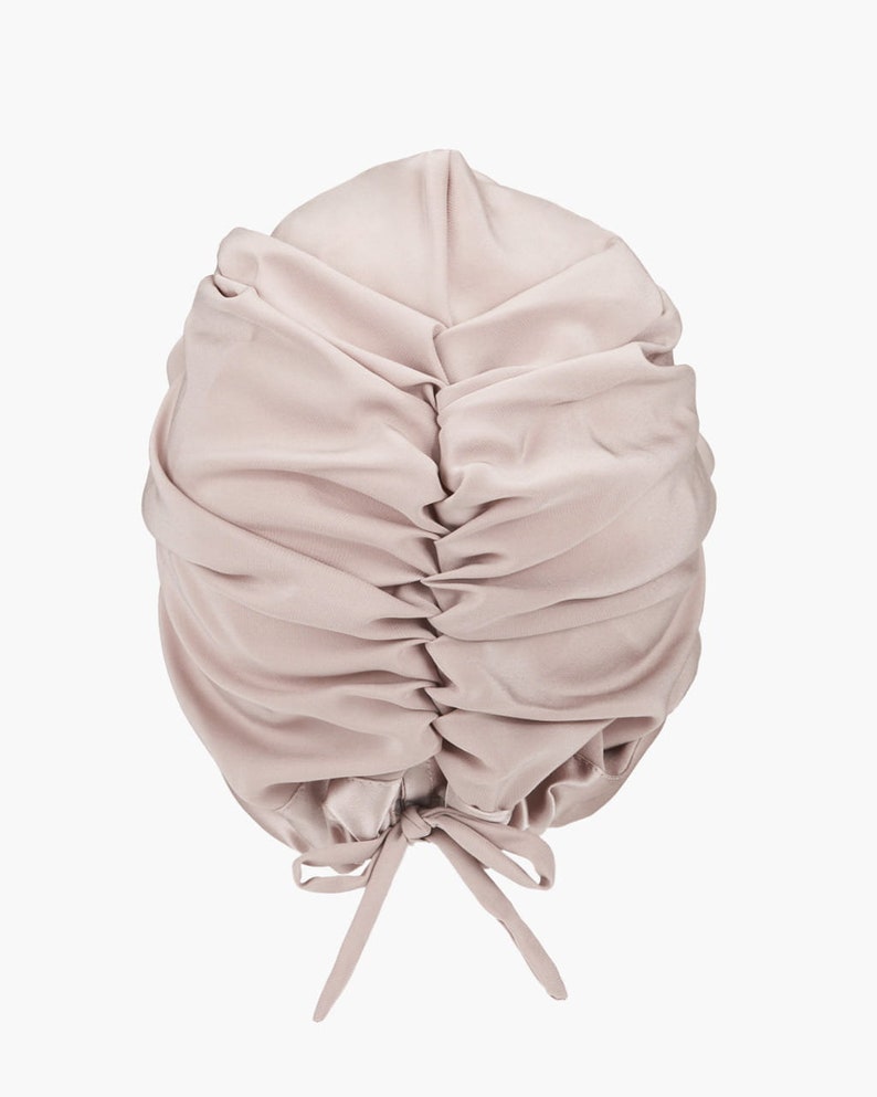 May include: A light pink satin sleep cap with a gathered top and a tie at the back.