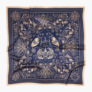 Op de afbeelding: Een marineblauwe bandana met een gouden paisley-patroon en twee vogels in het midden. De bandana heeft een bruine rand.