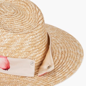Puede incluir: Un sombrero de paja de ala ancha con una cinta de estampado rosa y blanco alrededor de la corona.