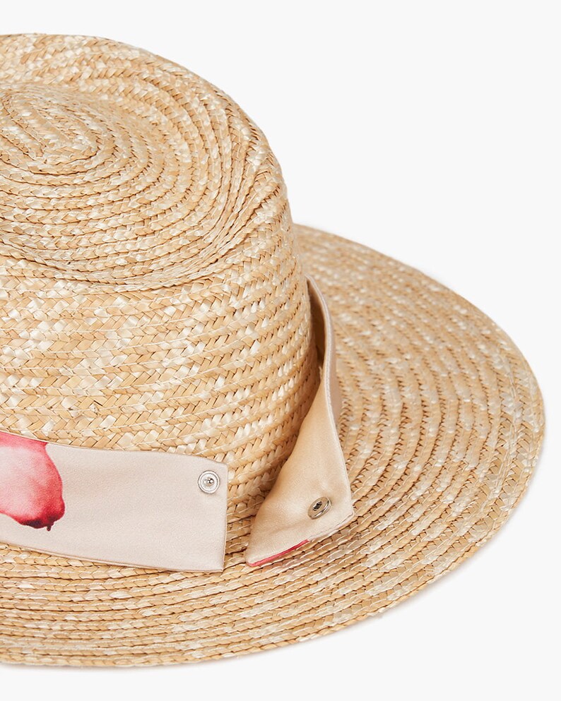 Puede incluir: Un sombrero de paja de ala ancha con una cinta de estampado rosa y blanco alrededor de la corona.
