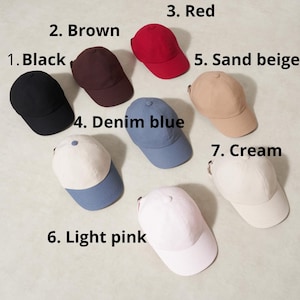 Op de afbeelding: Een verzameling van zeven baseballpetten in verschillende kleuren. De petten zijn zwart, bruin, rood, spijkerblauw, zandbeige, lichtroze en cr&egrave;me. Elke pet heeft een gebogen klep en een verstelbare stoffen band aan de achterkant.