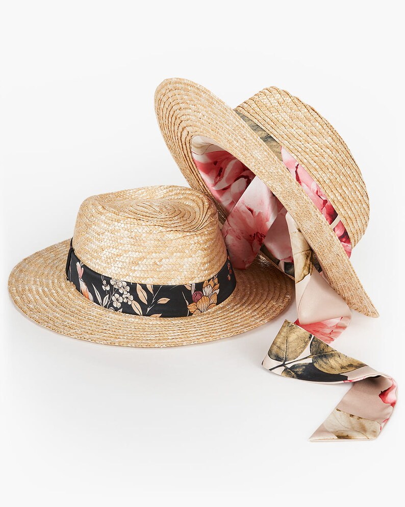 Puede incluir: Dos sombreros de paja con ribete de cinta floral. El sombrero de arriba tiene un forro floral rosa. El sombrero de abajo tiene una cinta floral negra.