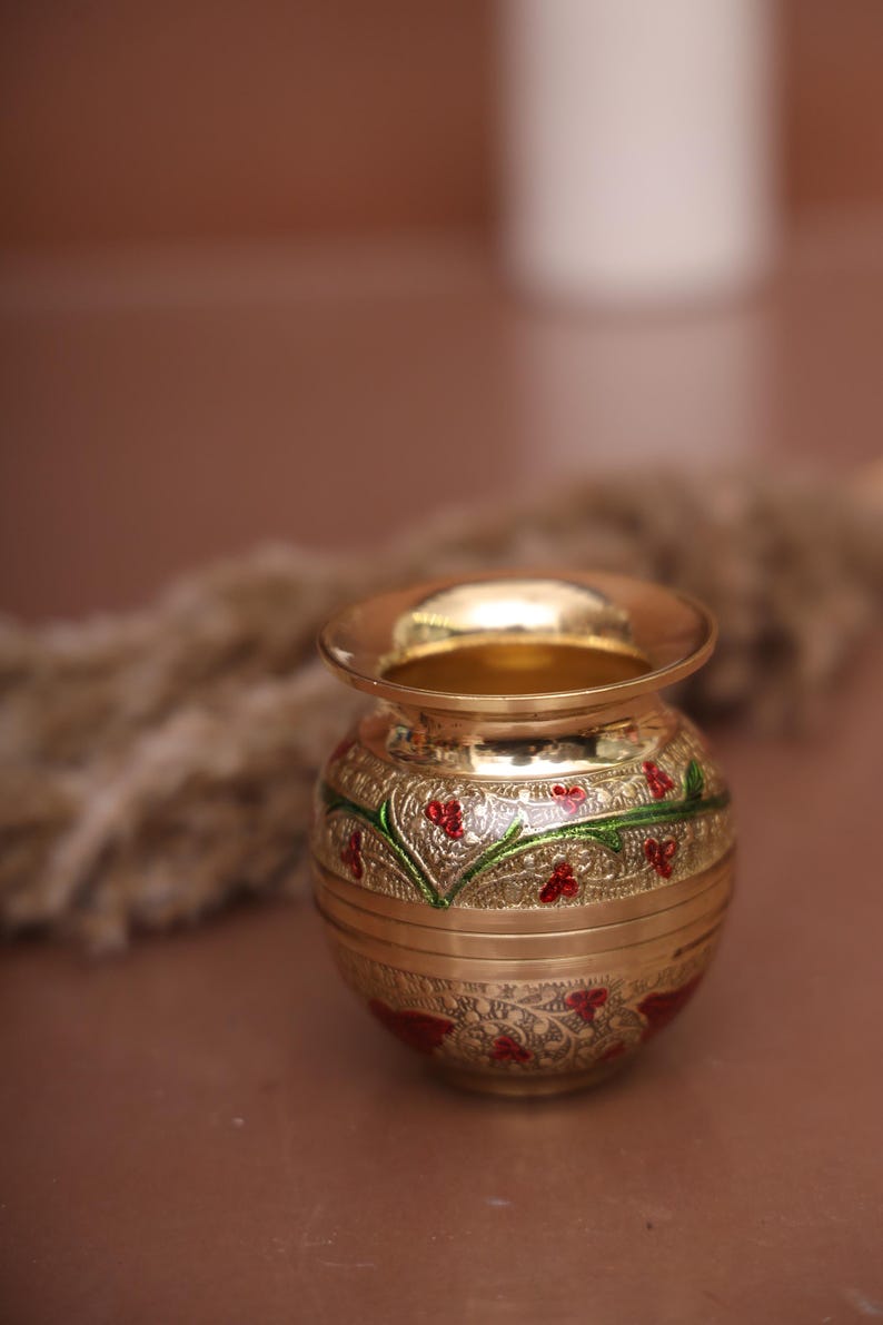 Puede incluir: Una peque&ntilde;a olla de metal dorada con intrincados dise&ntilde;os florales rojos y verdes. La olla est&aacute; decorada con un borde elevado y tiene un acabado liso y pulido.