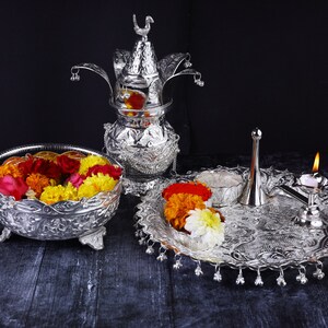 May include: A silver ceremonial set with a decorative pot, a bowl filled with colorful flowers, a small plate with flowers, a silver pitcher, and a lit candle.