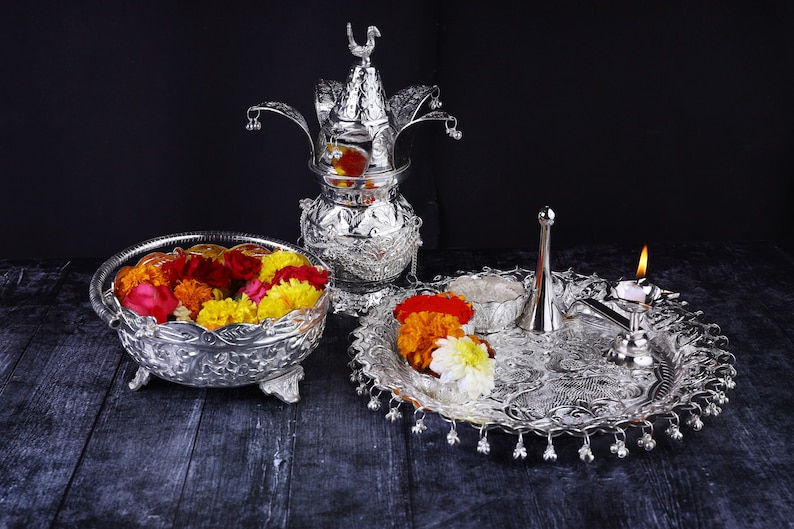 May include: A silver ceremonial set with a decorative pot, a bowl filled with colorful flowers, a small plate with flowers, a silver pitcher, and a lit candle.