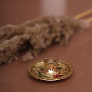 Puede incluir: Un quemador de incienso de metal dorado con un dise&ntilde;o floral decorativo. El quemador tiene una base redonda y una parte superior cil&iacute;ndrica alta con agujeros para varillas de incienso.