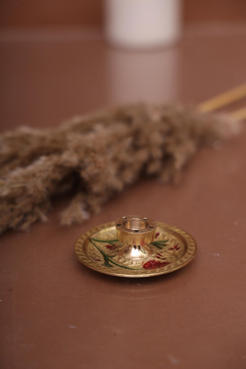 Puede incluir: Un quemador de incienso de metal dorado con un dise&ntilde;o floral decorativo. El quemador tiene una base redonda y una parte superior cil&iacute;ndrica alta con agujeros para varillas de incienso.