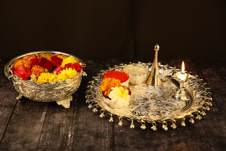 May include: A silver tray with a decorative design, holding a small bowl, a silver pitcher, a lit candle, and a bowl filled with yellow, orange, and red flowers.