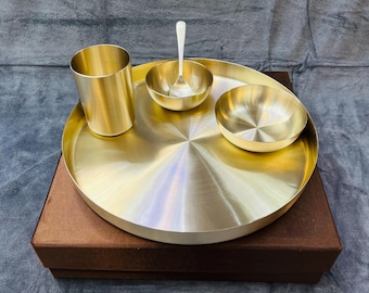 May include: A set of four gold-toned metal bowls and a cup, all on a brown velvet-covered box. The bowls are round and have a shiny finish. The cup is tall and cylindrical. The set is arranged in a circular pattern on the box.