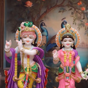 Puede incluir: Una estatua de m&aacute;rmol blanco de Krishna y Radha, una pareja de deidades hind&uacute;es, de pie juntos. Krishna sostiene una flauta y Radha sostiene una flor de loto. Las estatuas est&aacute;n decoradas con pintura colorida y joyas.