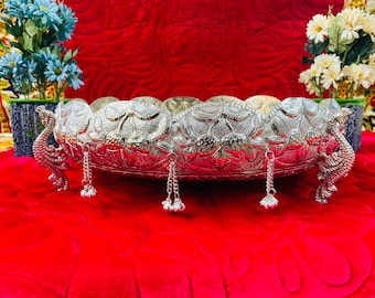 Puede incluir: Una bandeja de servir plateada con un diseño decorativo de pavo real y cadenas colgantes. La bandeja está sobre una superficie de terciopelo rojo.