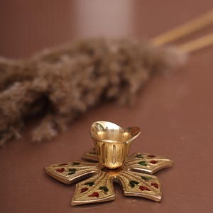 Puede incluir: Un portavelas de metal dorado con una base en forma de estrella y detalles de esmalte rojo y verde.
