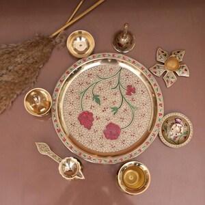 Puede incluir: Un plato de metal dorado con un dise&ntilde;o floral y acentos rojos. El plato est&aacute; rodeado de cuencos m&aacute;s peque&ntilde;os y una campana, todos hechos de metal dorado.