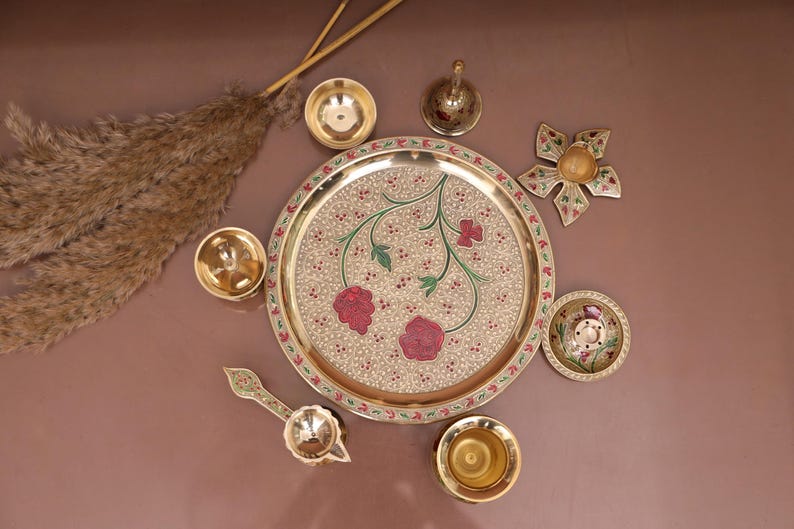 Puede incluir: Un plato de metal dorado con un dise&ntilde;o floral y acentos rojos. El plato est&aacute; rodeado de cuencos m&aacute;s peque&ntilde;os y una campana, todos hechos de metal dorado.
