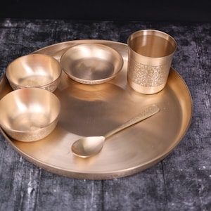 May include: A set of brass dinnerware, including a large plate, three bowls, a cup, and a spoon. All the pieces are decorated with intricate patterns.