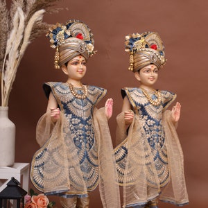 May include: Two intricately detailed figurines of deities, dressed in blue and gold robes with elaborate headwear, stand on wooden bases. The figurines are adorned with intricate embroidery and jewelry.