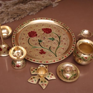 Puede incluir: Un juego de thali puja de metal dorado con un dise&ntilde;o floral decorativo. El juego incluye un plato, un diya, una campana, una cuchara, un kalash y un taz&oacute;n peque&ntilde;o.