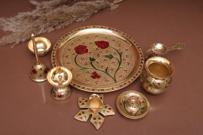 Puede incluir: Un juego de thali puja de metal dorado con un dise&ntilde;o floral decorativo. El juego incluye un plato, un diya, una campana, una cuchara, un kalash y un taz&oacute;n peque&ntilde;o.