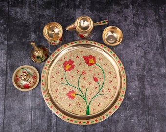 May include: A gold-colored metal serving tray with a floral design in red, green, and yellow. The tray is surrounded by smaller bowls and a pitcher, all with a similar gold finish.