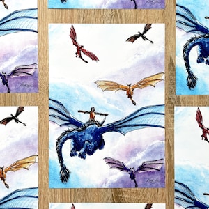 Peut inclure: Impressions d'art à l'aquarelle représentant des dragons volant dans un ciel nuageux. Les dragons sont représentés dans diverses couleurs, dont le bleu, le rouge, le violet et l'or. Chaque impression montre un dragon avec un cavalier, ajoutant un élément fantastique. Les impressions sont présentées sur une surface en bois.