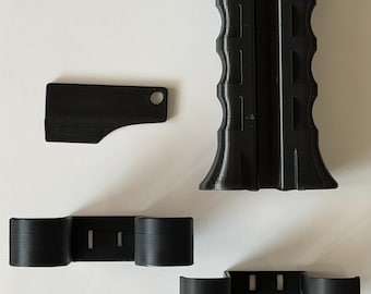 May include: Black 3D-printed components, including a handle with a textured grip, a small rectangular piece with a hole, and two sets of cylindrical supports. The parts are arranged on a white surface.