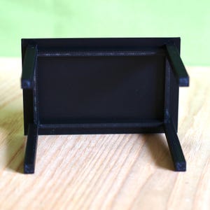 May include: A small, rectangular black table shown from an inverted perspective, revealing its flat underside and four straight, slender legs extending upward. The surface has a matte, textured finish consistent with 3D printed construction.