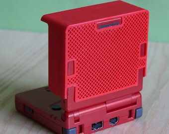 May include: A red handheld gaming console with a hinged design, featuring a bright red protective cover with a textured grid pattern attached to the top lid. The base of the device shows grey hinge accents and ports along the back edge.