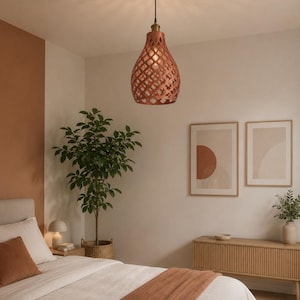 May include: A copper-coloured pendant light with a lattice-style geometric cutout pattern, suspended from a black ceiling mount by a thin cord. The light fixture emits a warm glow, casting intricate shadow patterns onto the ceiling above.