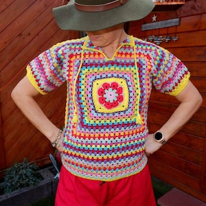 May include: A colorful crochet top with a square design in the center. The top is made with a variety of colors, including yellow, pink, blue, green, and red. The top has short sleeves and a scoop neck.