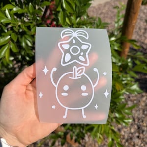 May include: A white, translucent sticker featuring a cartoon apple character with arms raised, topped with a star and bow design. The sticker also includes four diamond-shaped accents.