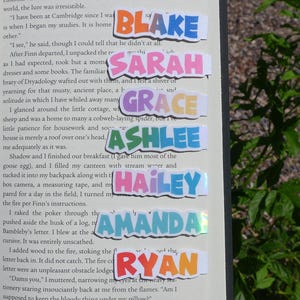 May include: Colorful name stickers in various fonts and colors, including Blake, Sarah, Grace, Ashlee, Hailey, Amanda, and Ryan. The stickers are placed on the pages of a book.