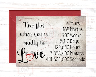May include: A greeting card with a red envelope features the text "Time flies when you're madly in Love." The card includes a list of time increments, such as 14 years, 168 months, and 5,110 days, with a heart-shaped clock graphic.