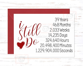 May include: A red and white card with the text "i still do" in red cursive font. A red heart is drawn next to the word "do". The card also includes a list of time measurements in years, months, weeks, days, hours, minutes, and seconds.