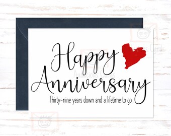 May include: A white card with black text that reads "Happy Anniversary" with a red heart graphic and the text "Thirty-nine years down and a lifetime to go".