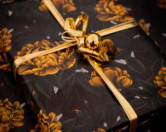 May include: A black gift box with a gold ribbon and gold ornaments. The box is wrapped in paper with a floral pattern in shades of gold and green.