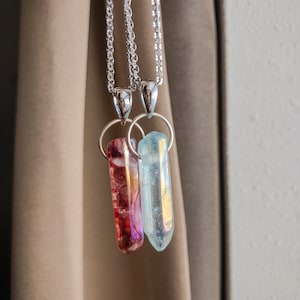 Può includere: Due catene d'argento con ciondoli di cristallo. Un ciondolo è un cristallo trasparente e sfaccettato, l'altro è un cristallo rosso e viola.