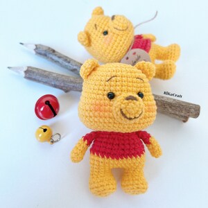 Pu&ograve; includere: Due orsi Winnie the Pooh all'uncinetto, uno con una camicia rossa e l'altro con un'etichetta marrone che dice "fatto a mano".